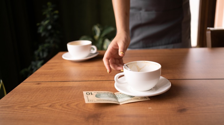 Server's hand taking cup with $10 on cafe's table