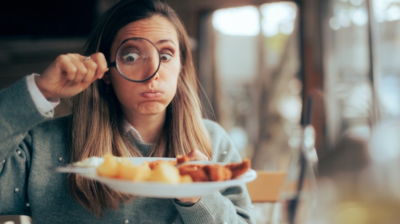 Funny food critic checking the restaurant dish with a magnifying glass