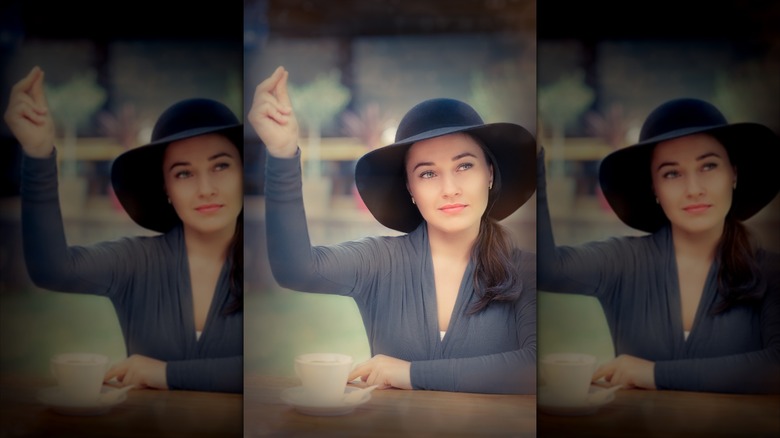 Young woman wearing a broad hat snaps her fingers to call the waitstaff