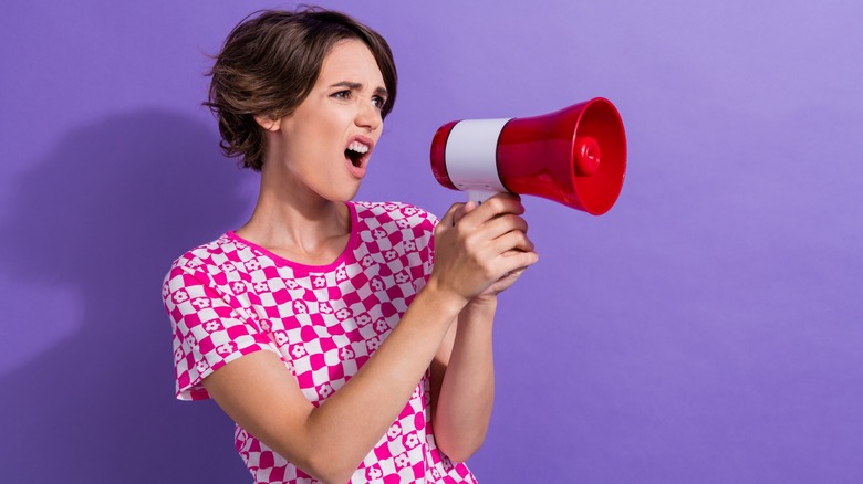 Woman shouting into a loudspeaker on a purple background