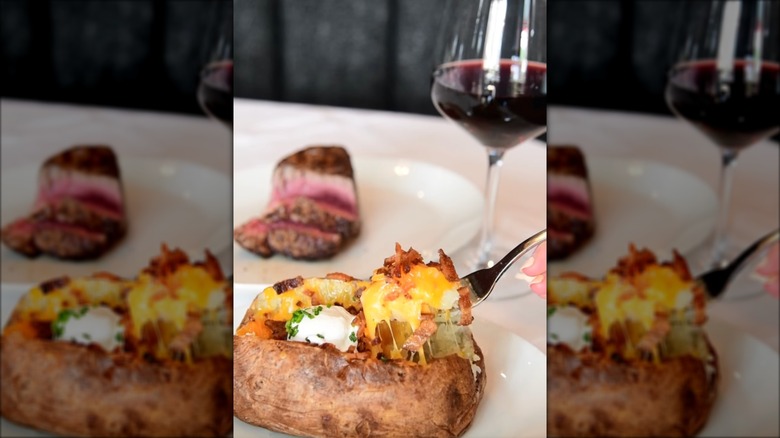Del Frisco's Double Eagle Steakhouse loaded baked potato with steak and glass of red wine in background