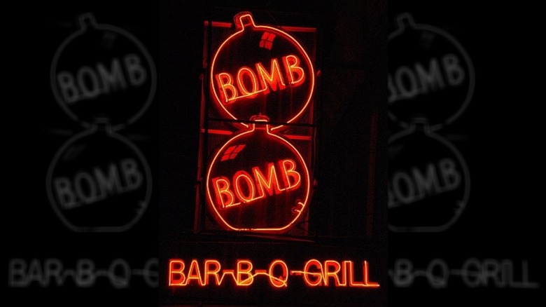 The exterior red neon sign for Bomb Bomb at night; two cartoonish bombs stacked on each other with "bomb" on the inside of each  and "bar-b-q-grill" underneath