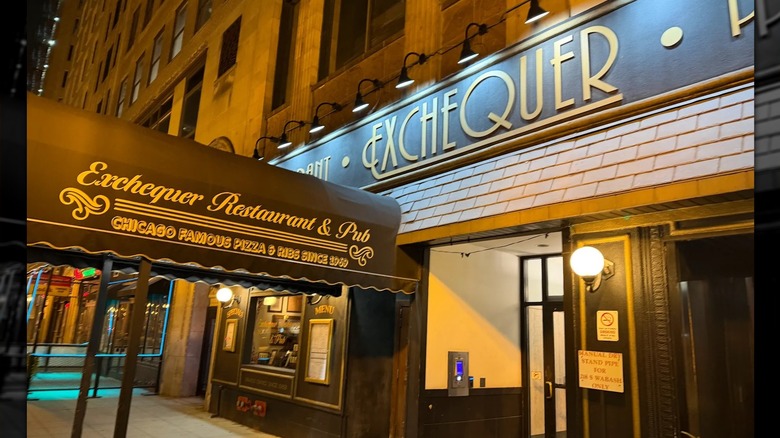 The exterior of the Exchequer: tall brick building on a Chicago city street; brown awning reading "Exchequer Restaurant & Pub Chicago Famous Pizza & Ribs Since 1969" in gold leads into the door; brown sign on building reads "Exchequer" in gold