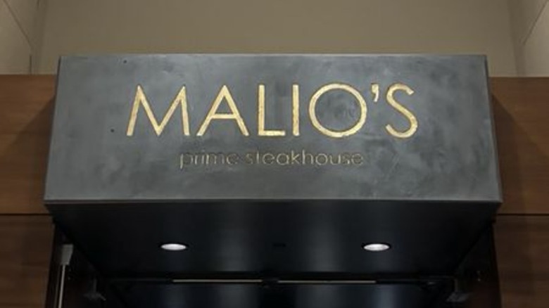 A dark stone sign that reads "Malio's Prim Steakhouse" in gold set above a dark wood-trimmed doorway