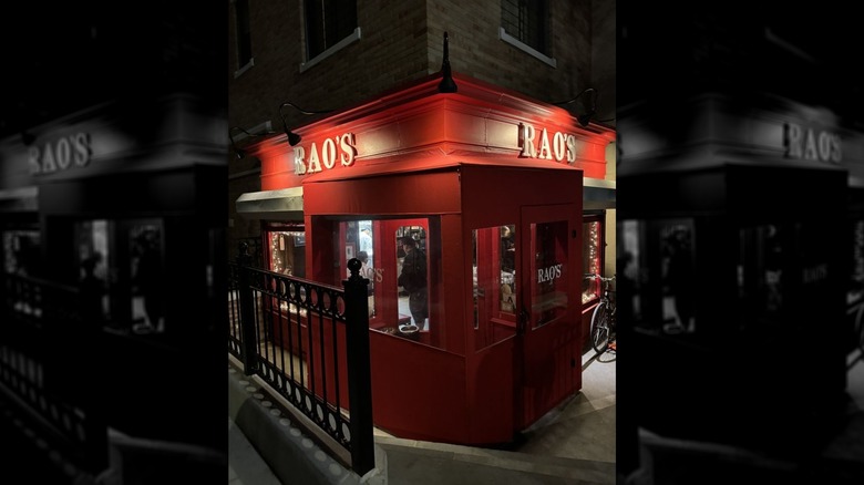 The exterior of Rao's at night; corner building, corner vantage point; with exterior and white "Rao's" signs on each side; windows on each side