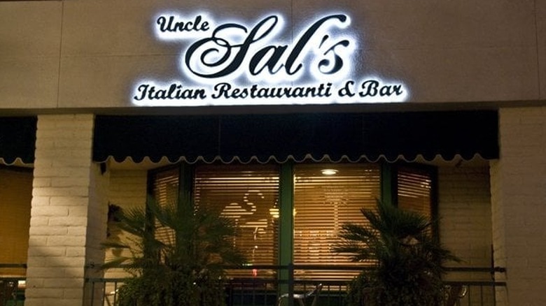 The exterior of Uncle Sal's at night; beige concrete building with brick pillars surround a large window with a green awning; lit sign reads: "Uncle Sal's Italian Restauranti & Bar"