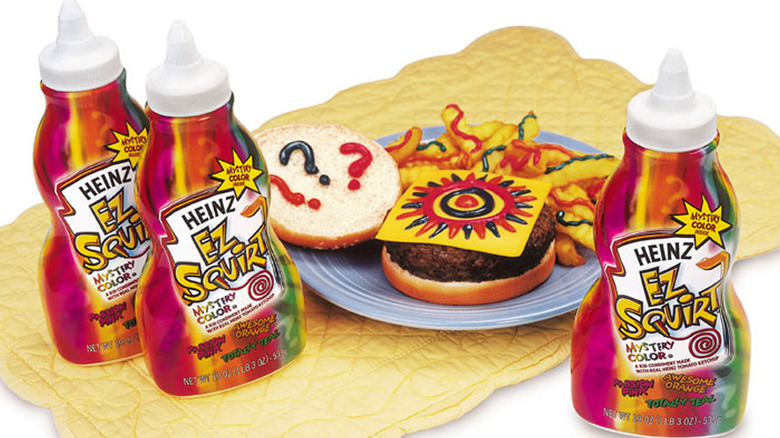 Heinz EZ Squirt Ketchup Bottles beside a burger and plate of fries covered in colorful ketchup designs