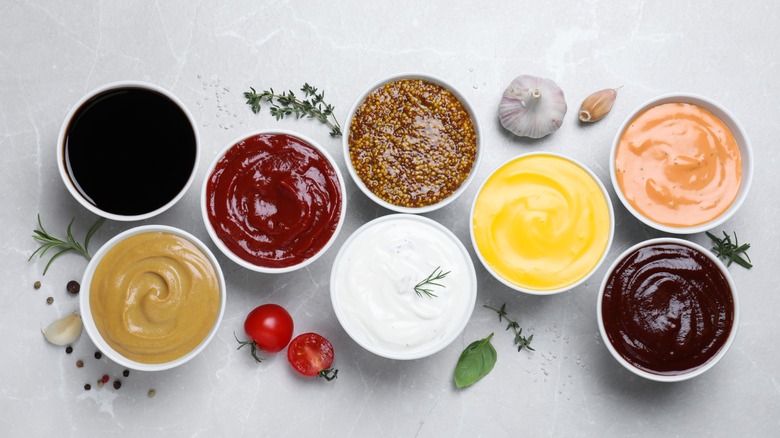 Many different condiments in ramekins on light grey table, flat lay
