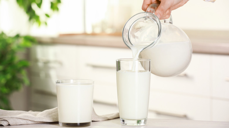 milk being poured into glasses from a pitcher, held by a person off screen in a clean, white kitchen