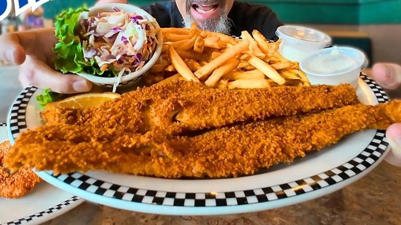 Hands holding up a plate of Black Bear Diner fried fish with French fries and a side of cole slaw.