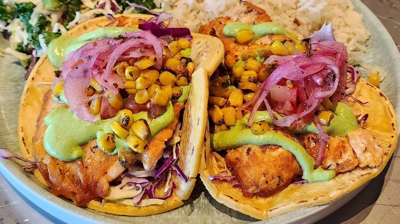 A plate with two fish tacos with corn, onion and green sauce.