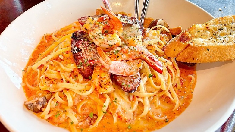 A large plate of pasta in sauce, covered in cooked shrimp.