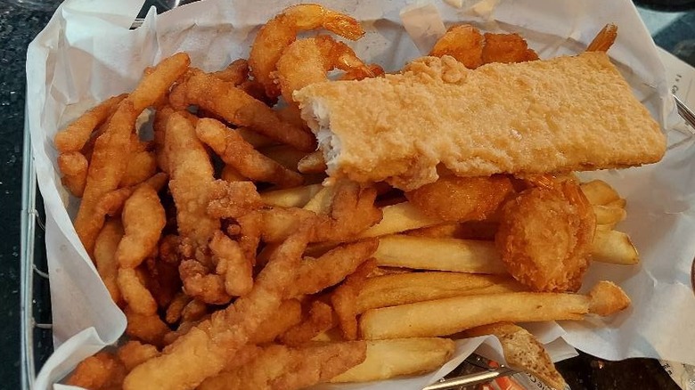 A full basket of fried clams, shrimp and fish on top of a pile of fries.