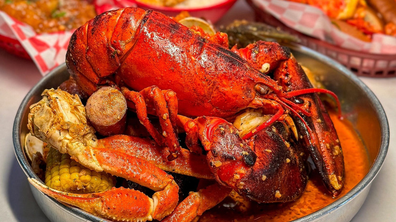 An Angry Crab seafood boil, with a large lobster sitting in a bowl on top of a pile of crab legs, sausage and corn.