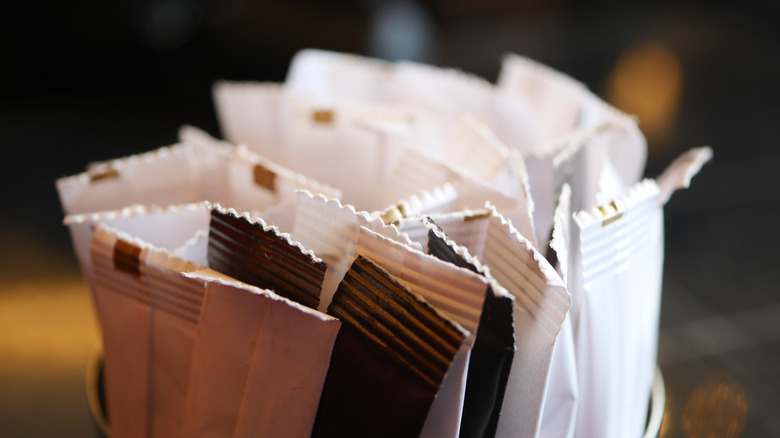 A close-up view of assorted sugar and sweetener packets in shades of white, brown, and black, neatly arranged in a holder.