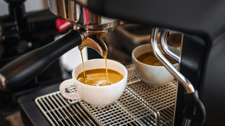 An espresso machine pouring golden-brown espresso into a white ceramic cup.