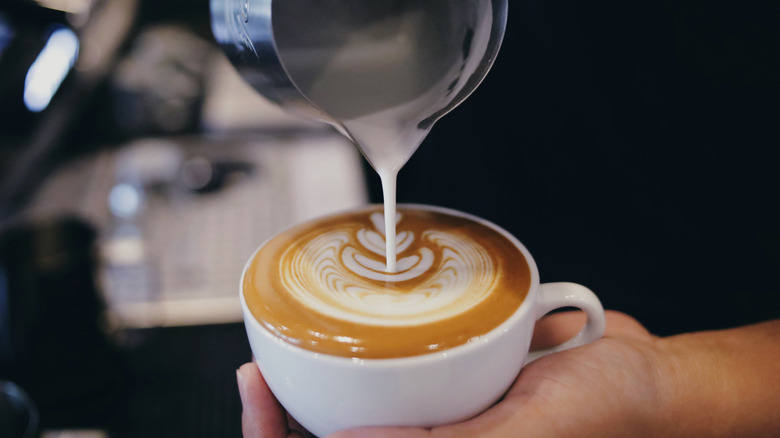A barista pouring velvety steamed milk into a white cup, forming latte art.