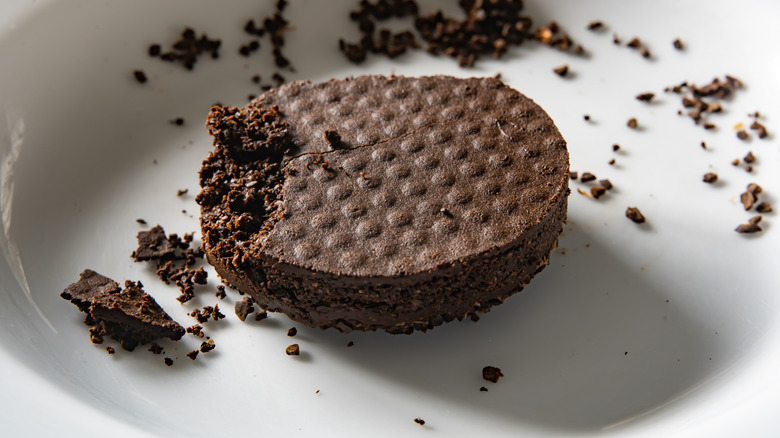 A close-up of a used espresso puck on a white plate surrounded by scattered coffee grounds.