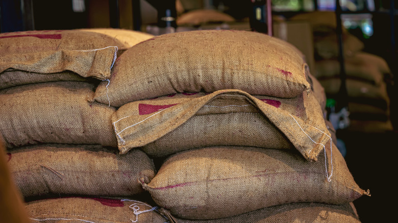 Stacked burlap sacks filled with coffee beans and stored in a dimly lit roasting facility.