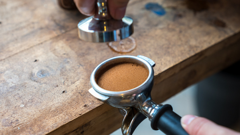 A barista tamping espresso grounds evenly into a portafilter using a metal tamper
