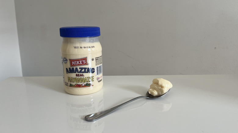 A jar of Mike's amazing mayonnaise next to a spoon on a white table