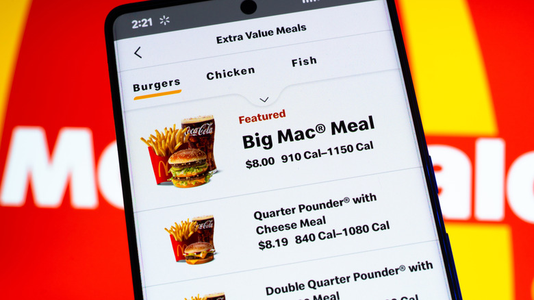 McDonald's menu items on a food delivery app on a smartphone being held in front of the McDonald's logo