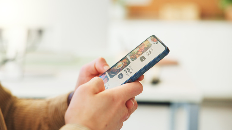 Hands scrolling through a food delivery app on a smartphone against a blurred background