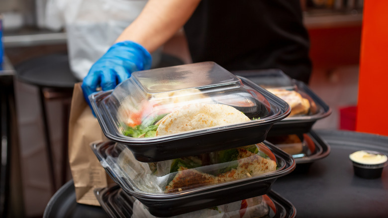 A close-up of a restaurant employee wearing gloves and packing up a to-go order