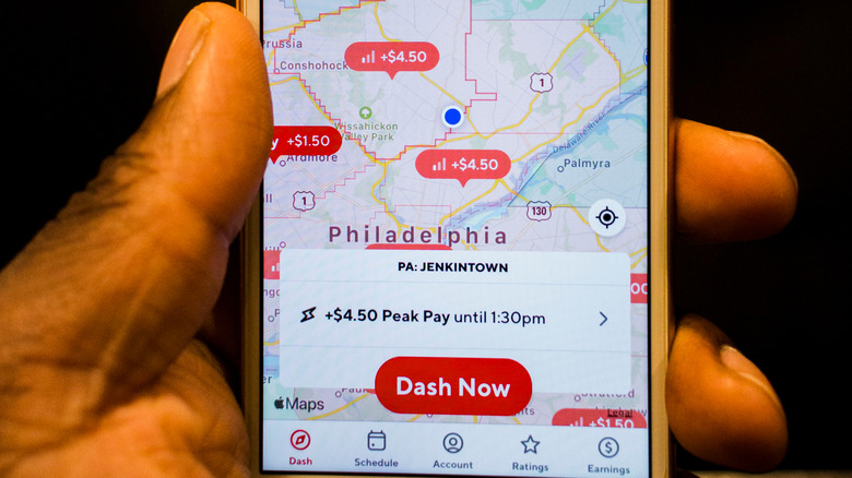 A hand holding a smartphone open to the DoorDash dasher app