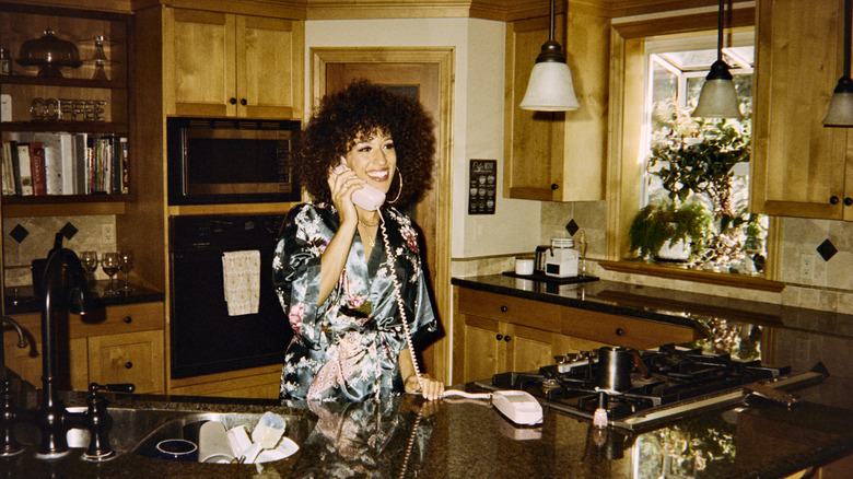 A woman in a retro kitchen with plants and wood paneling
