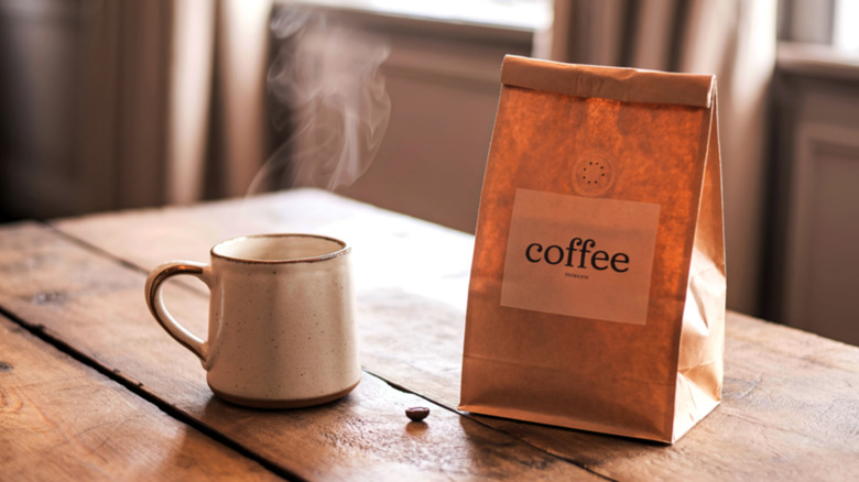Bag of coffee next to cup of coffee on table