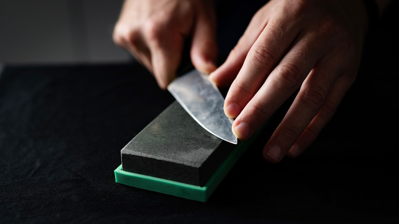 Two hands guide a chef's knife along a stone surface for sharpening.
