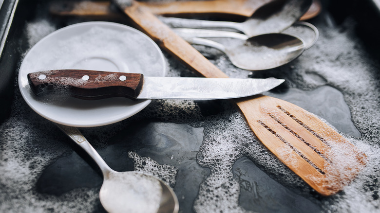 A chef's knife on top of a pile of soapy wet dishes in the sink