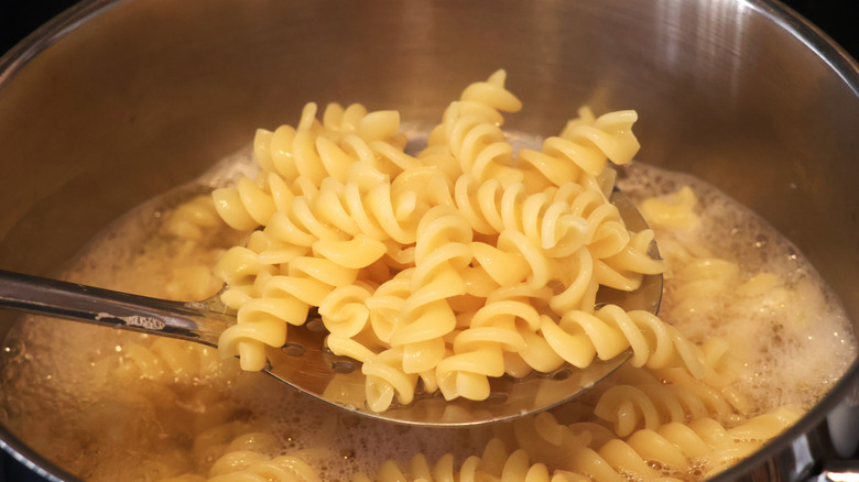 A spoonful of cooked rotini pasta over a boiling pot