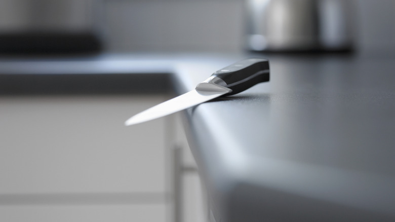 A chef's knife teeters precariously on the edge of a gray counter