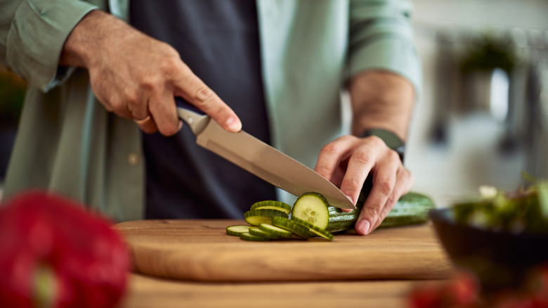 Hands cut a cucumber on a stable cutting board