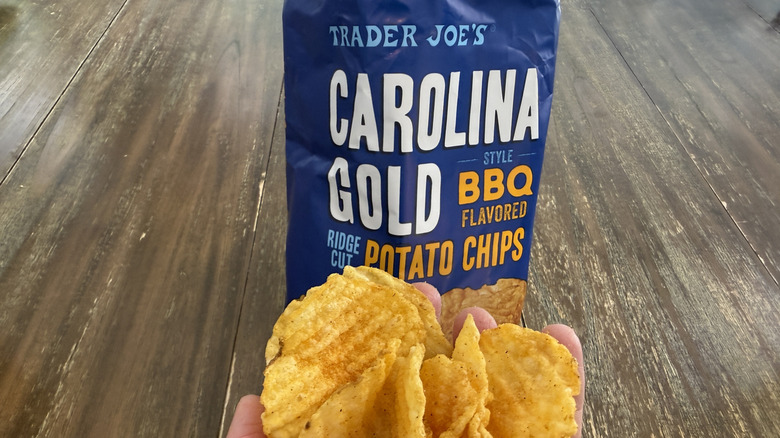 Trader Joe's Carolina Gold Style BBQ Flavored Ridge Cut Potato Chips on wooden table and a handful of them
