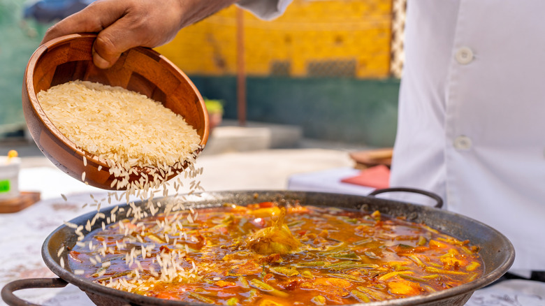 Chef adding rice to a large paella pan