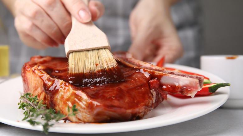 person brushing marinade over raw steak