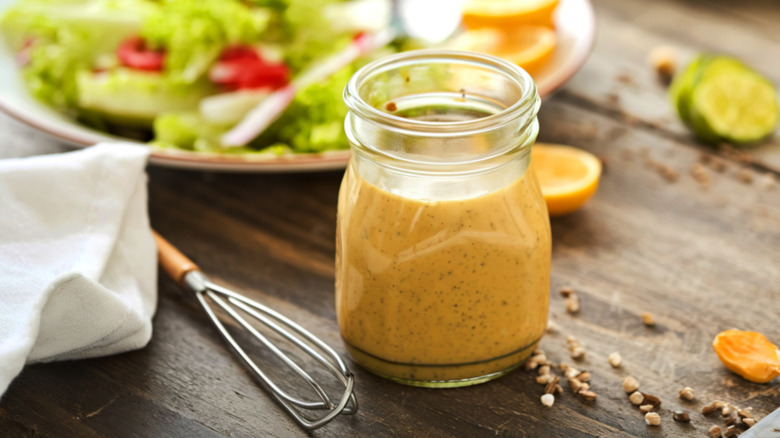 yellow salad dressing in clear jar on table with whisk