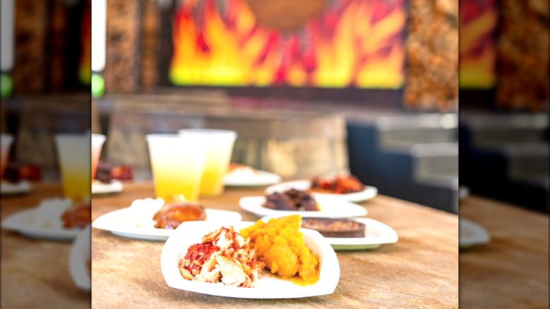 A few plates of BBQ food and drinks on a wooden table
