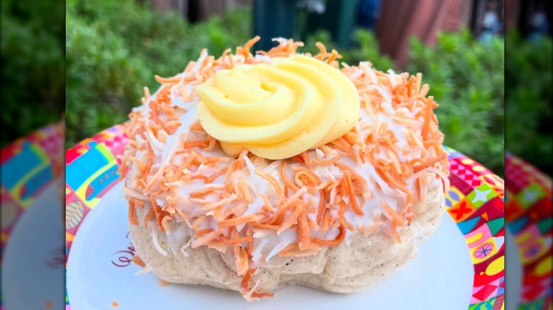 A coconut and cream-covered small cake on a paper plate