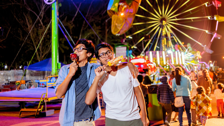 Two young men eating snacks at a carnival.