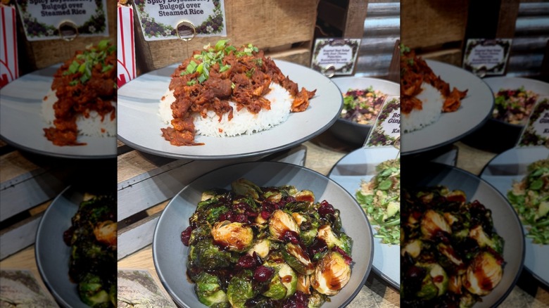Three plates of food arranged in front of small label signs, including spicy boysenberry pork bulgogi over steamed rice