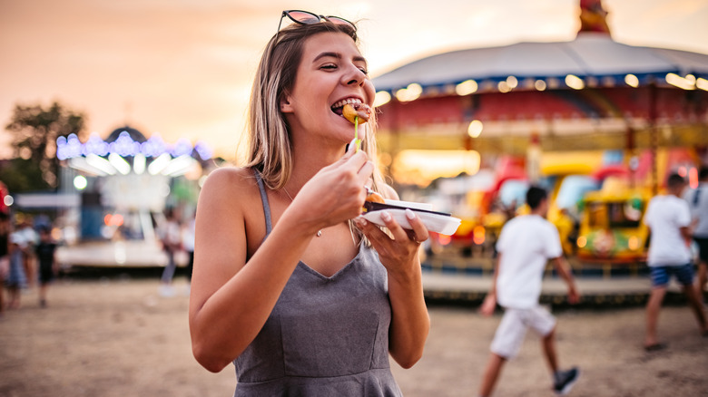 A smiling woman eating a snack at a fair