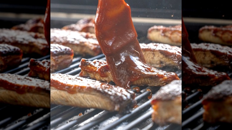 Multiple pieces of salmon on the grill, and one is being slathered with red glaze