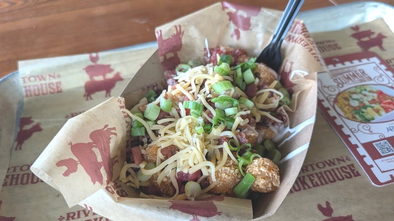 BBQ tater tots topped with shredded cheese and green onions in a restaurant container