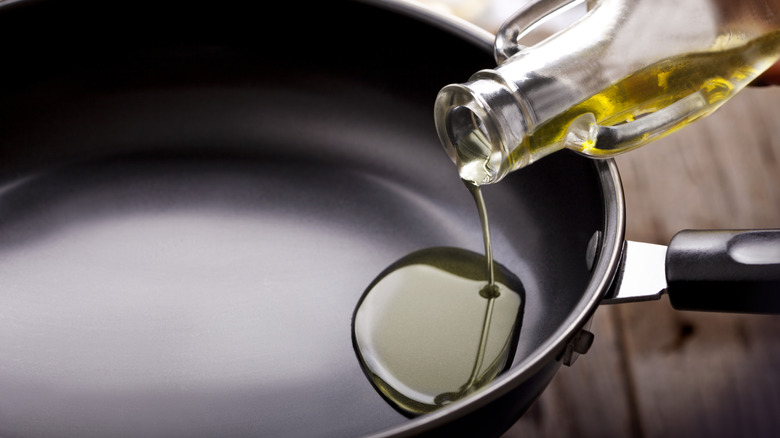 a glass bottle of cooking oil being poured into a black skillet