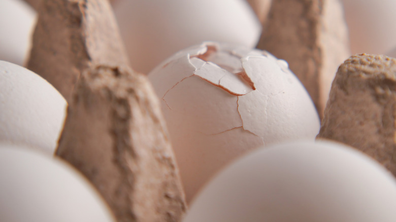 a close up of a cracked egg in an egg carton with other intact eggs