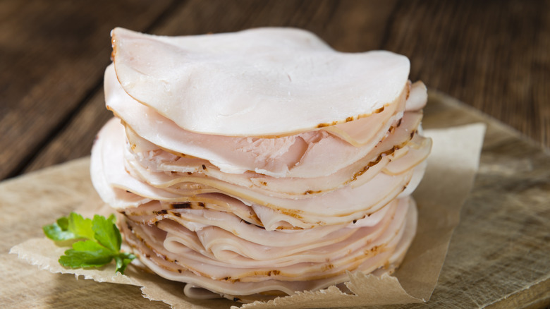 a stack of thinly sliced deli meat on a piece of paper on top of a wooden cutting board